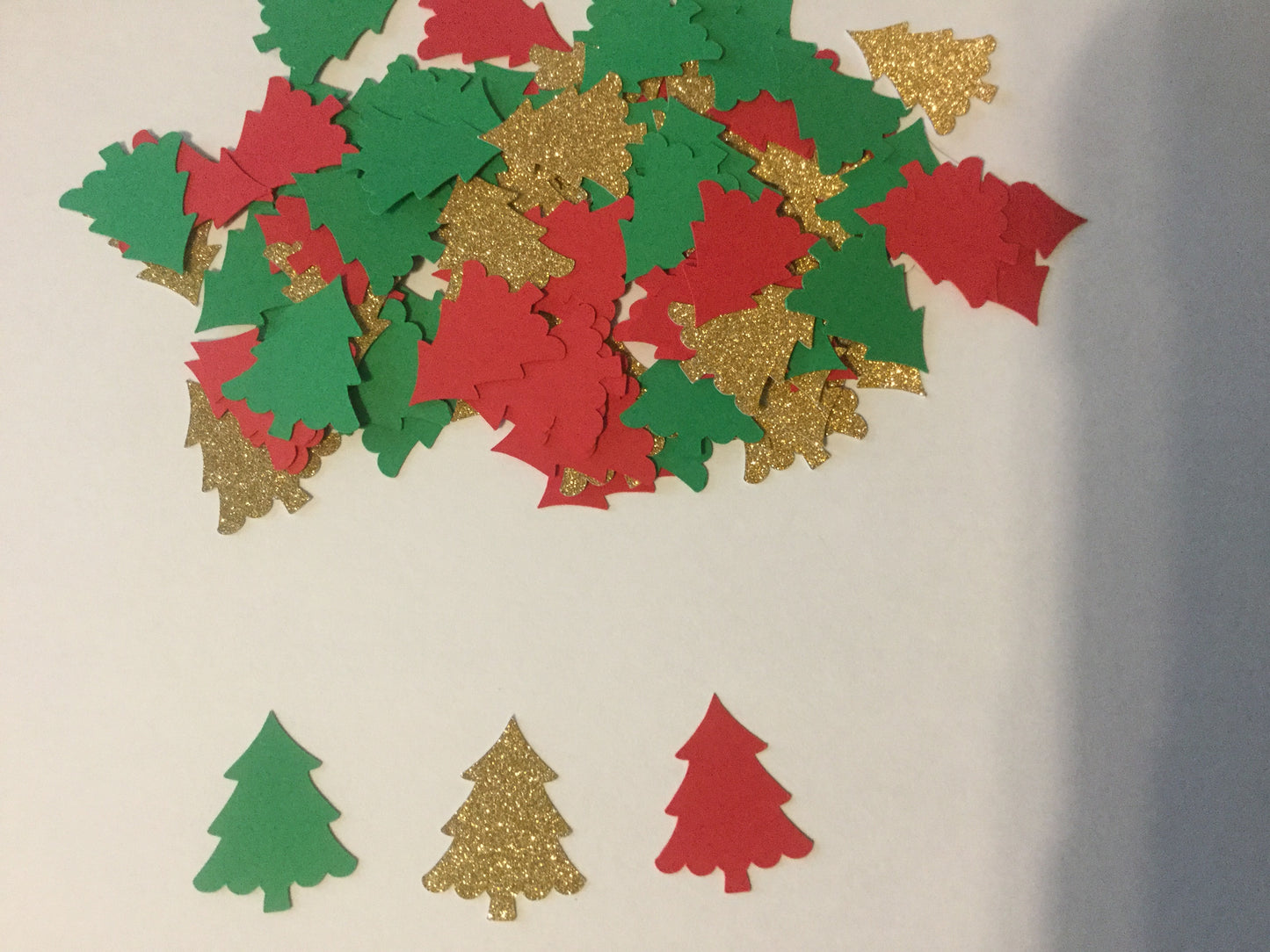 Decorative cutout shapes of Christmas trees in red, green, and gold on a beige background.