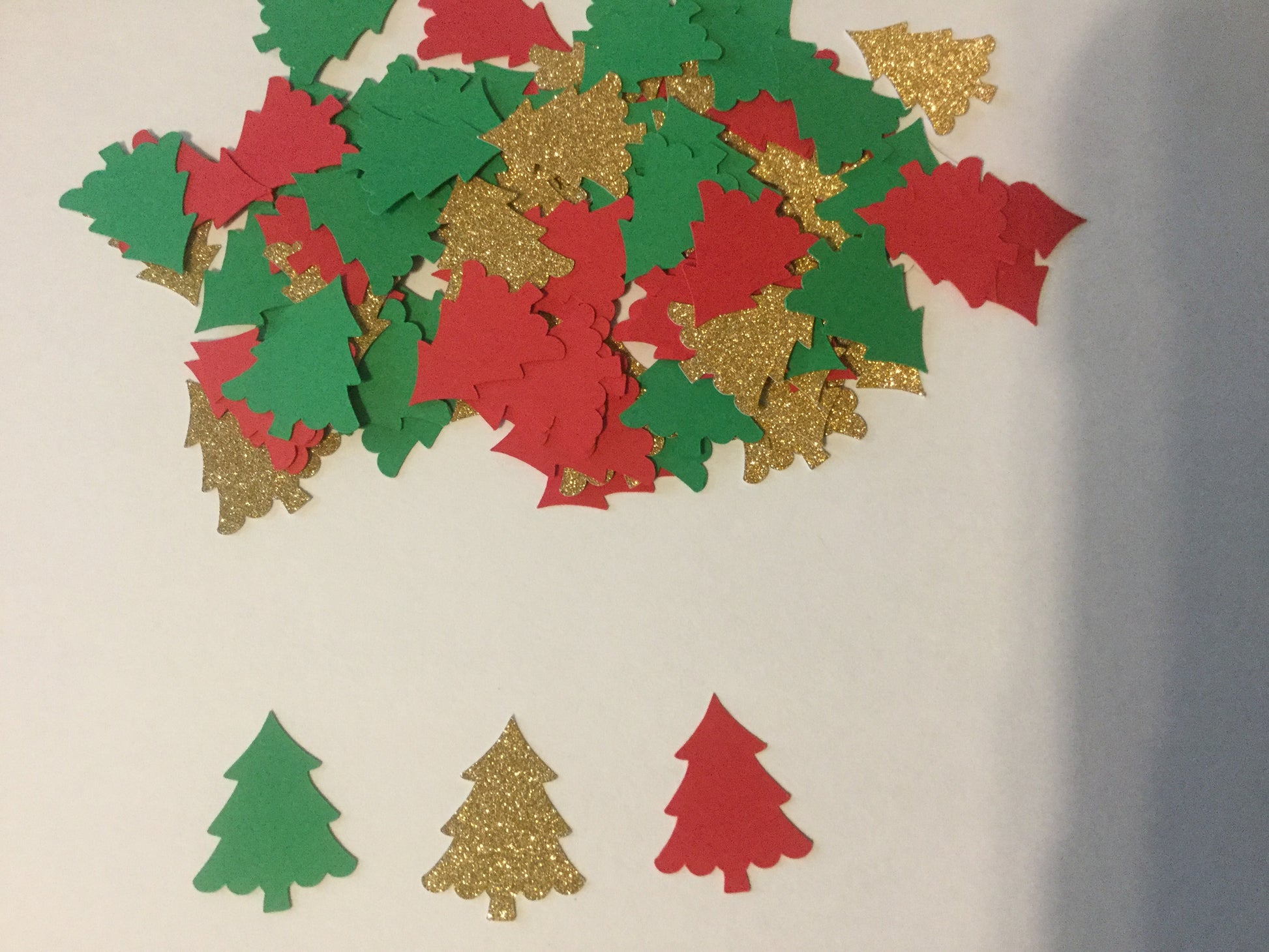 Decorative cutout shapes of Christmas trees in red, green, and gold on a beige background.