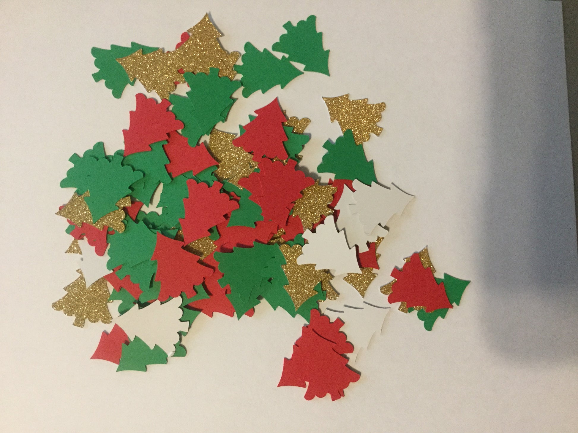 Decorative cutout shapes of Christmas trees in red, green, and gold on a beige background.